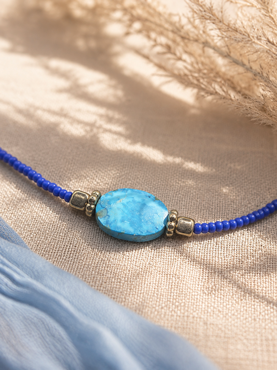 Detailfoto van een turquoise sierkraal in een handgemaakte blauwe kralenketting.