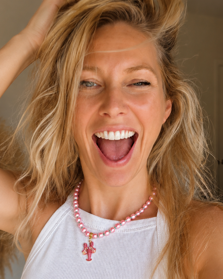 Model draagt een handgemaakte roze kralenketting met goudkleurige kreeft bedel, gestyled in een boho outfit.