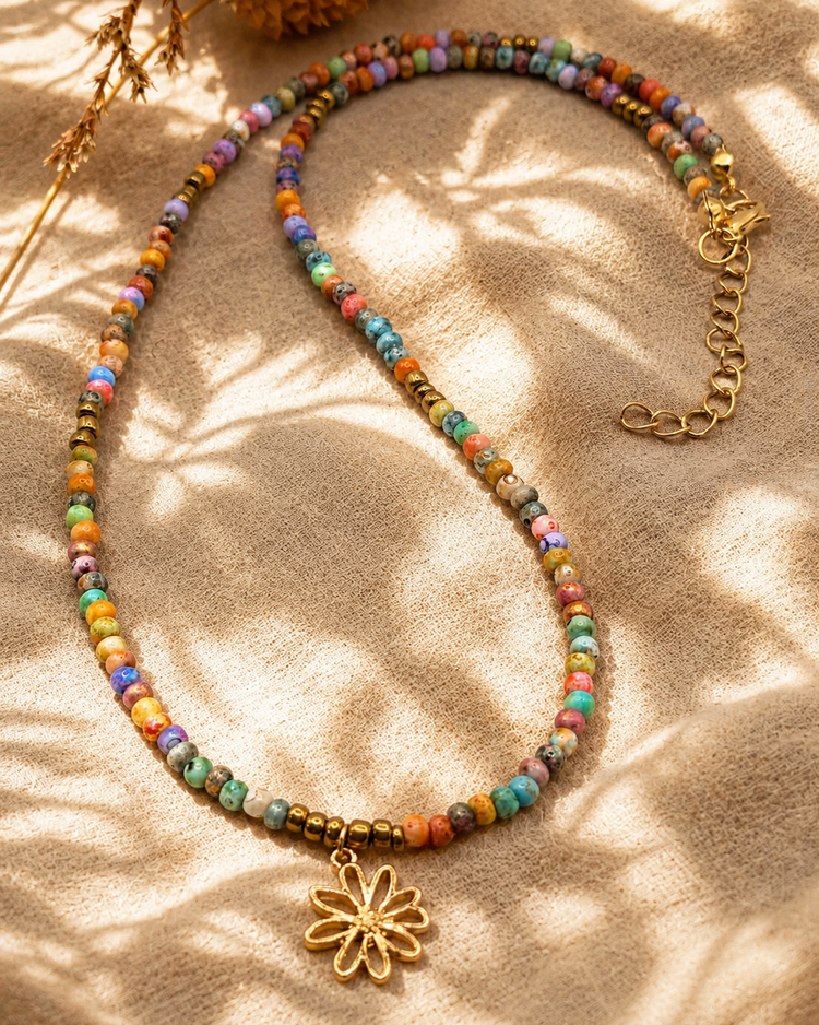 Kleurrijke natuursteen kralenketting met gouden bloembedel op een linnen doek in boho beach stijl.