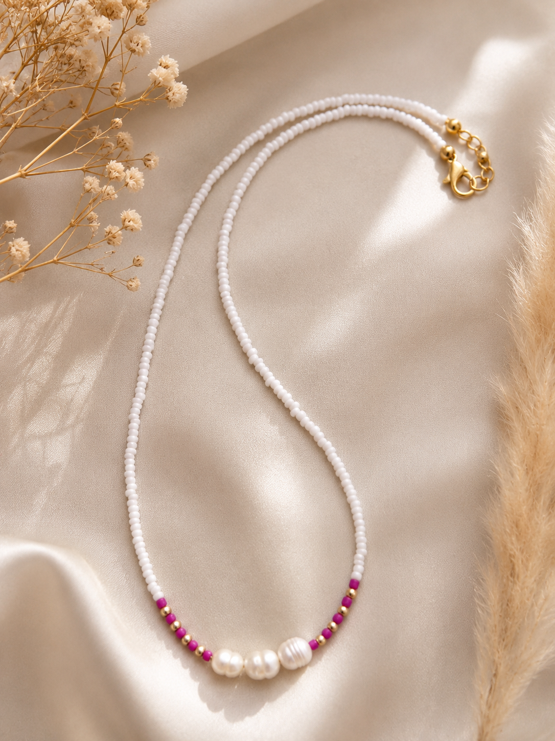 Handgemaakte witte kralenketting met drie zoetwaterparels, fuchsia accenten en goudkleurige details op een champagnekleurige satijnen ondergrond