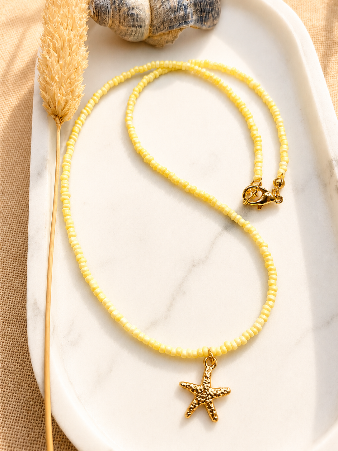 op een marmeren ondergrond ligt een botergele zachte kralenketting met een gouden sluiting en een gouden zeester bedel