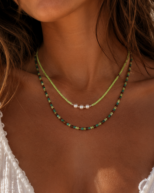 Model draagt een handgemaakte dubbele groene kralenketting met drie parels en fijne glaskralen.