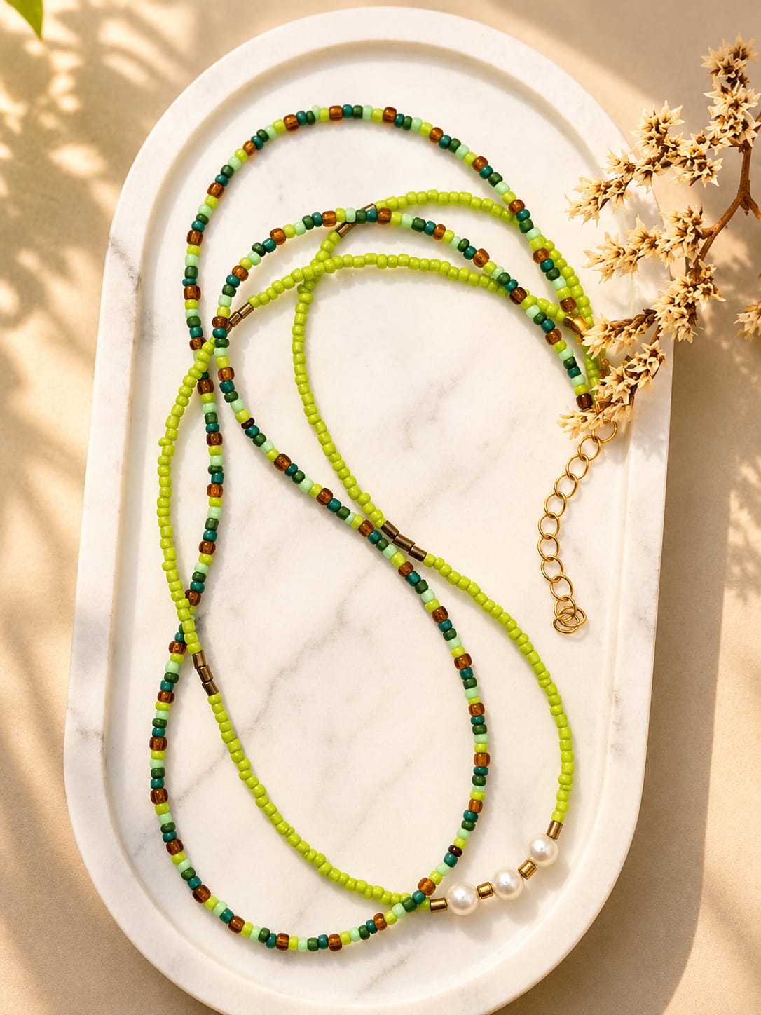 Handgemaakte dubbele groene kralenketting met parels op een lichte marmeren ondergrond.