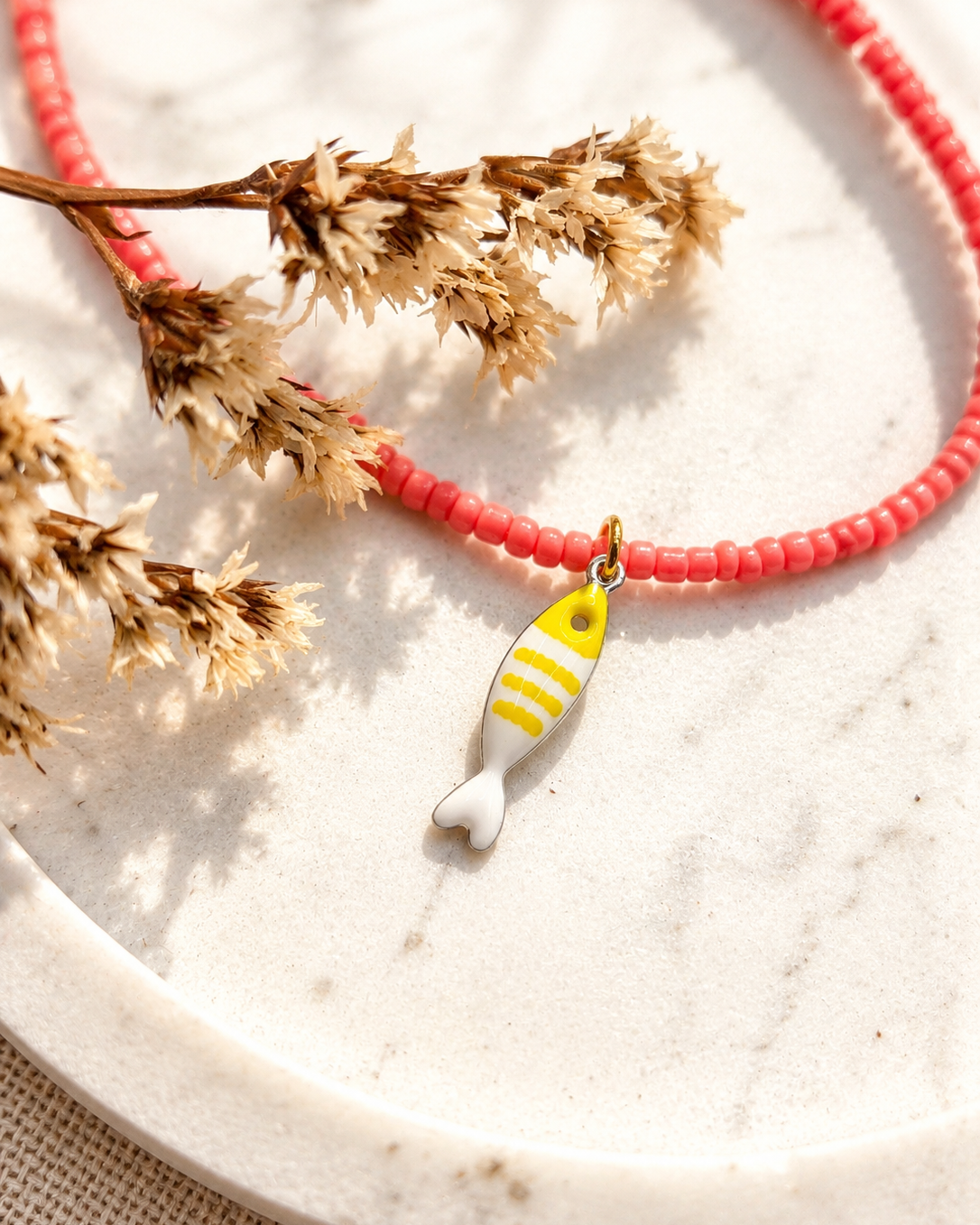 close up van een geel visjeshangertje aan een roze ketting op een marmeren ondergrond