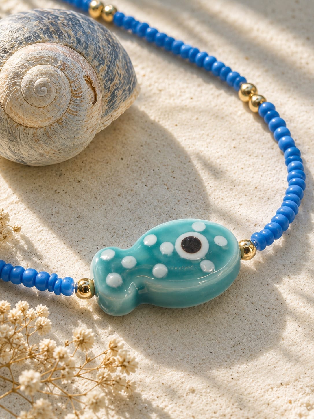 Detailfoto van de Azure Fish blauwe boho kralenketting met turquoise glazen visje en goudkleurige kralen.