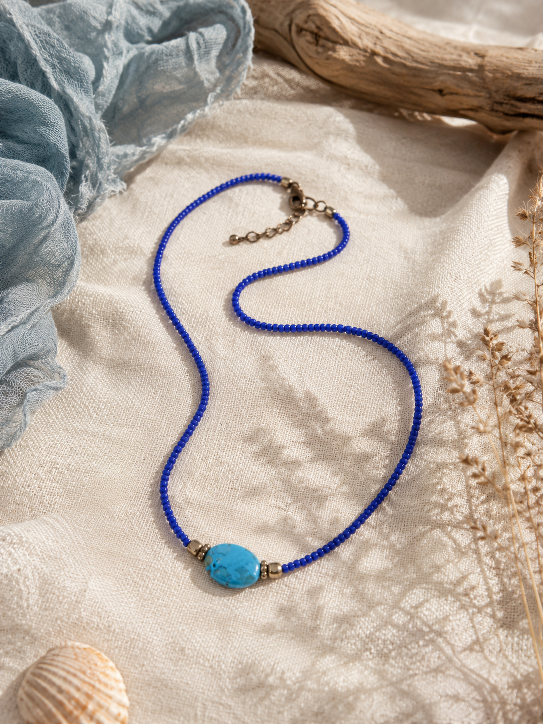 Handgemaakte blauwe kralenketting met turquoise sierkraal en goudkleurige accenten.