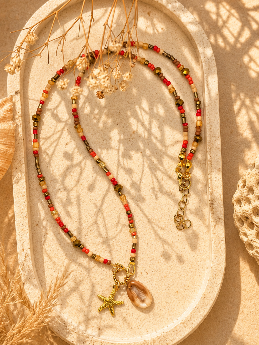Boho beach kralenketting met schelp, gouden zeester en warme kralen op een lichte zonnige ondergrond van Blissh.