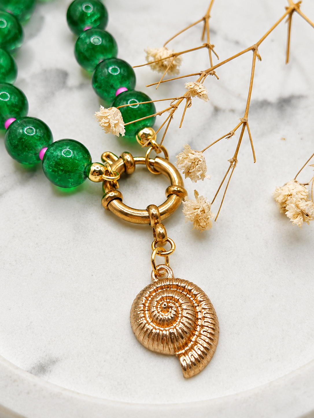 een close-up van een schelpbedel aan een boeislot van een smaragdgroene kralenketting met roze kleine kraaltjes