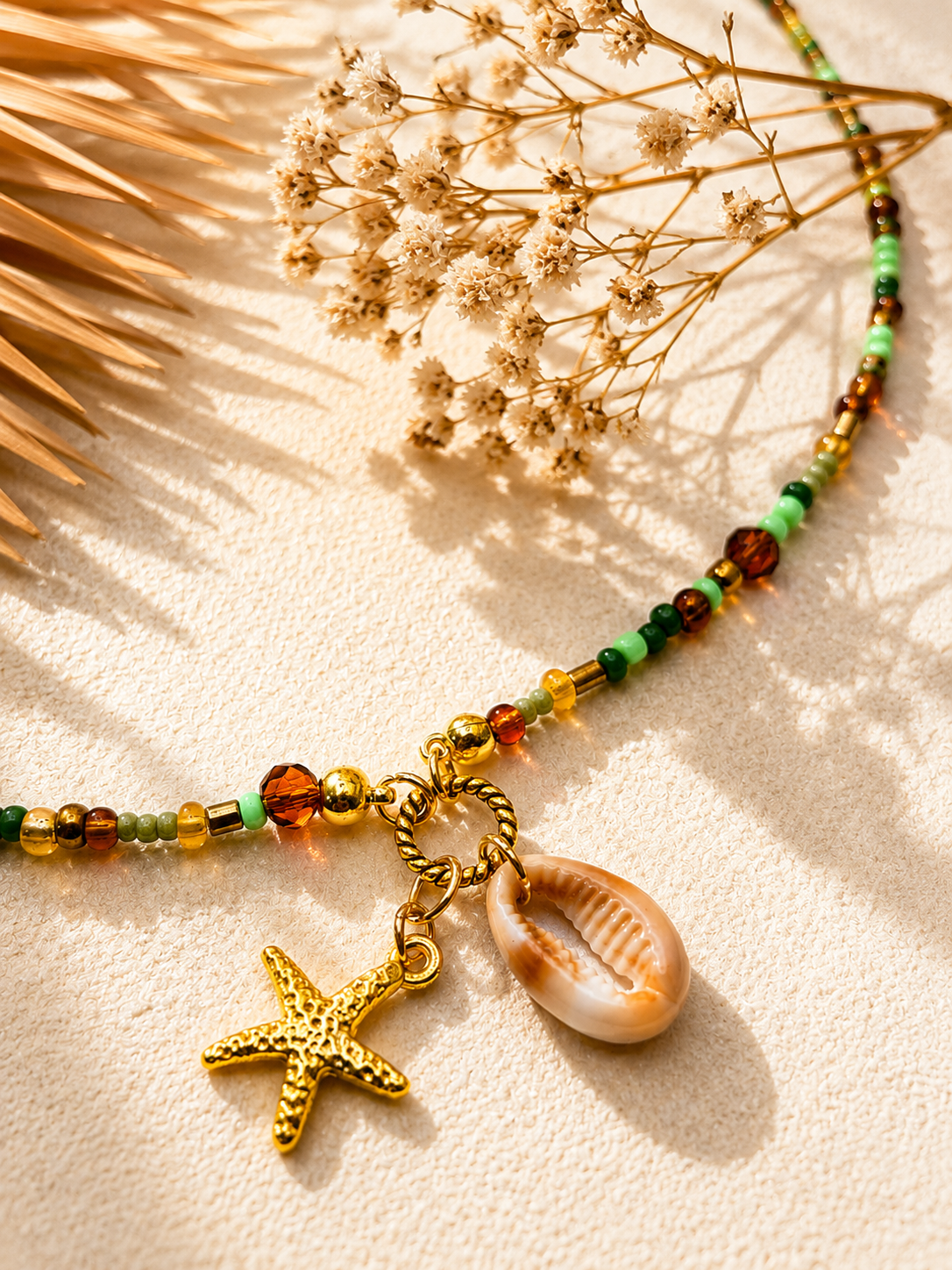 Detail van een handgemaakte groene kralenketting met goudkleurige zeester en natuurlijke schelpbedel van Blissh.