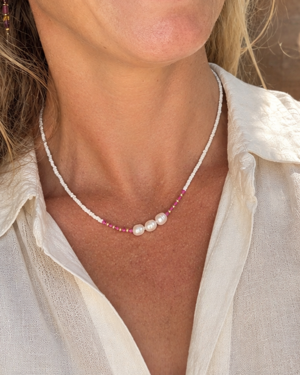 Zongebruind model met een handgemaakte witte kralenketting van glaskraaltjes, drie zoetwaterparels en fuchsia accenten.