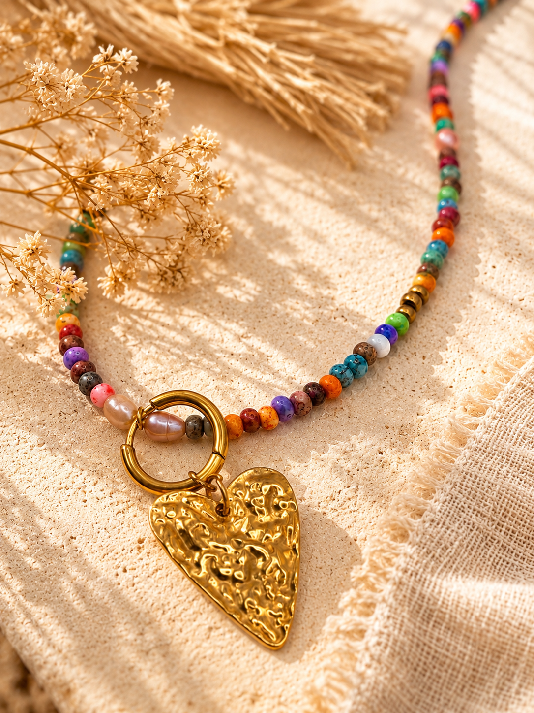Detail van een handgemaakte kleurrijke kralenketting met grote goudkleurige hartbedel en zoetwaterparels van Blissh.