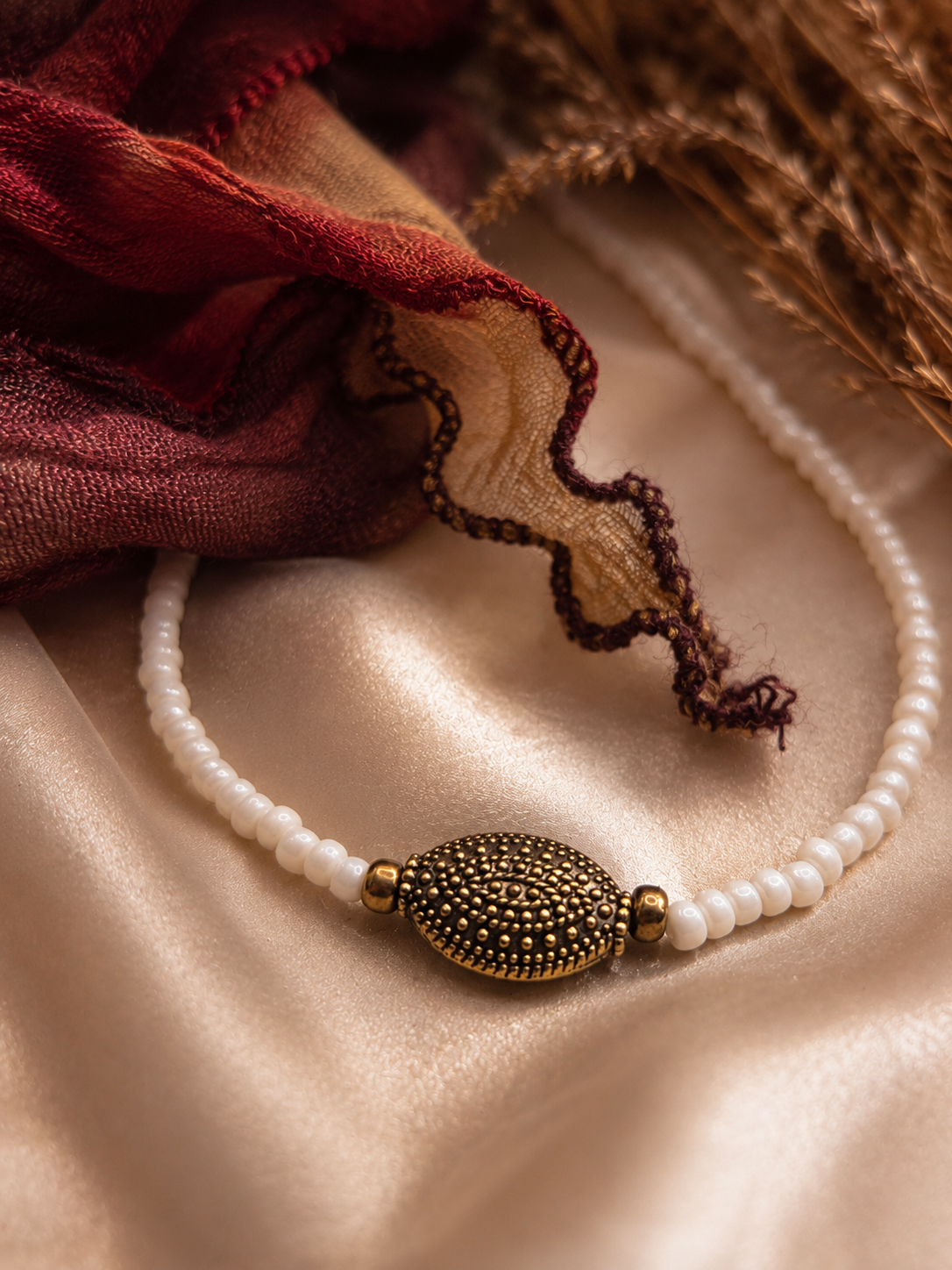 Close-up van een handgemaakte witte kralenketting met goudkleurig ovaal accent.