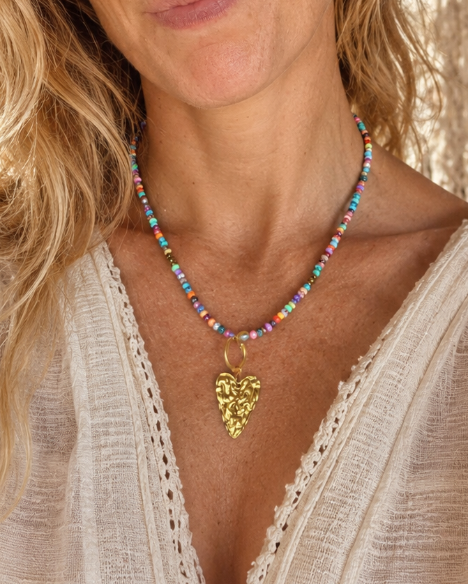 Model draagt een handgemaakte kleurrijke kralenketting met grote goudkleurige hartbedel van Blissh.
