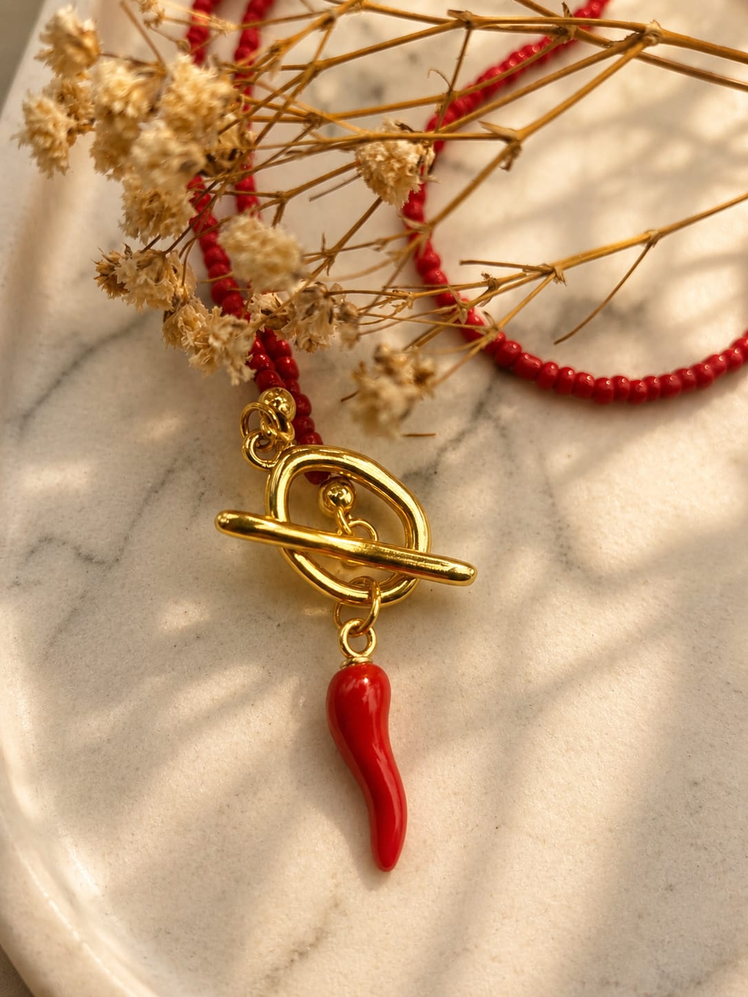 Detail van een rode kralenketting met goudkleurige toggle-sluiting en Italiaans gelukshoorntje.