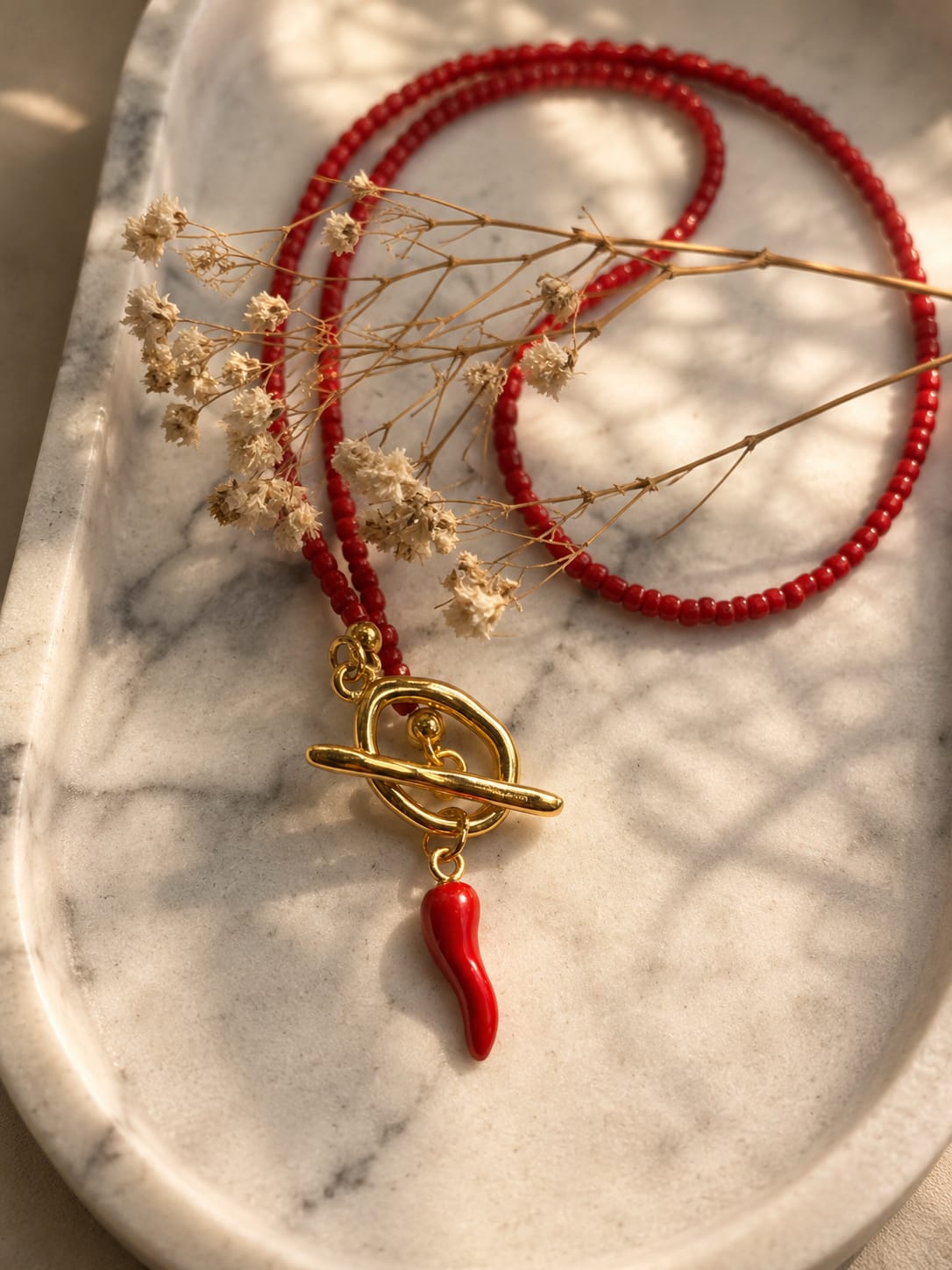 Handgemaakte rode kralenketting met gouden toggle-sluiting en rode corno-bedel.