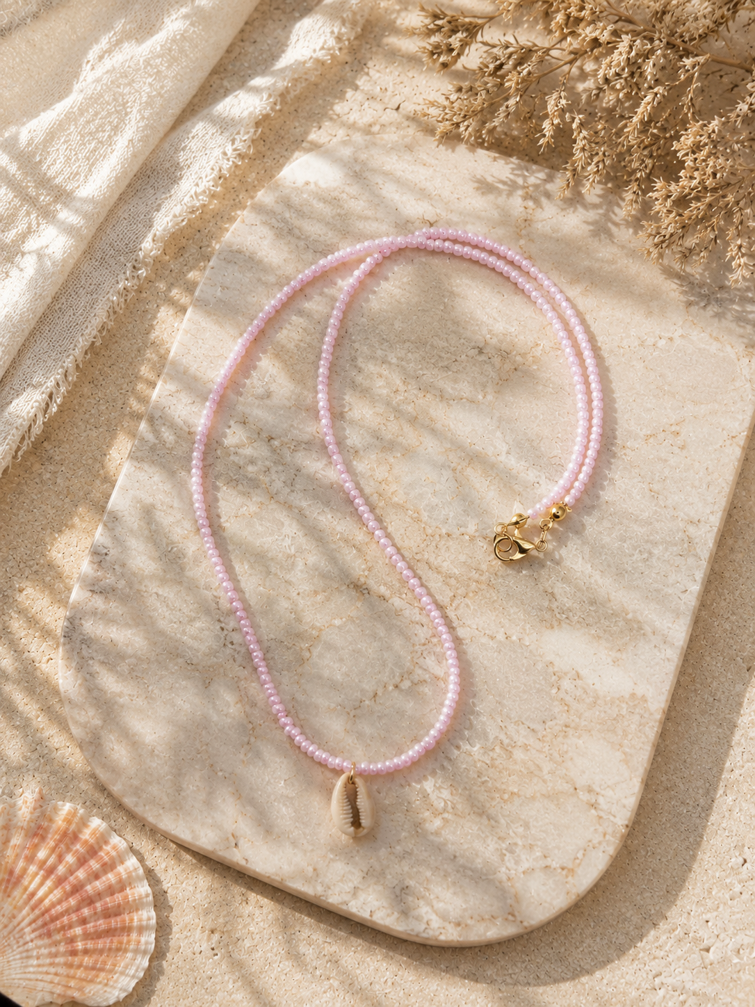 Handgemaakte roze kralenketting met natuurlijke kauri schelp, verstelbare sluiting en goudkleurige details.