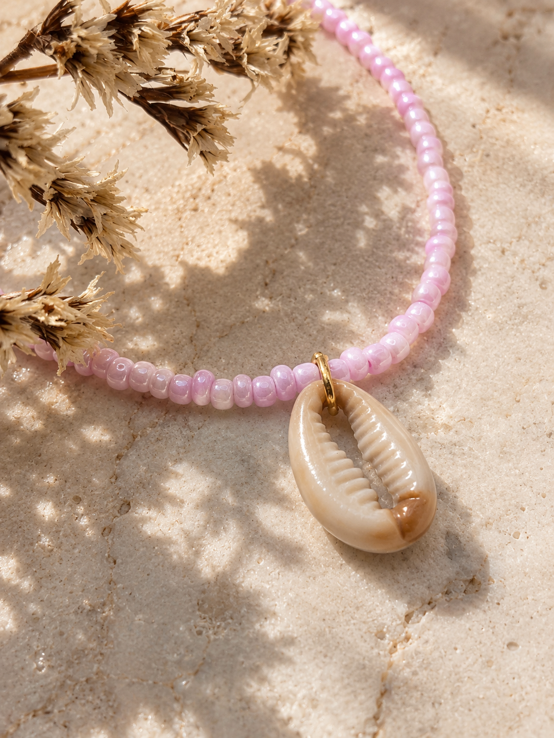 Detailfoto van een handgemaakte roze kralenketting met natuurlijke kauri schelp en goudkleurige accenten.