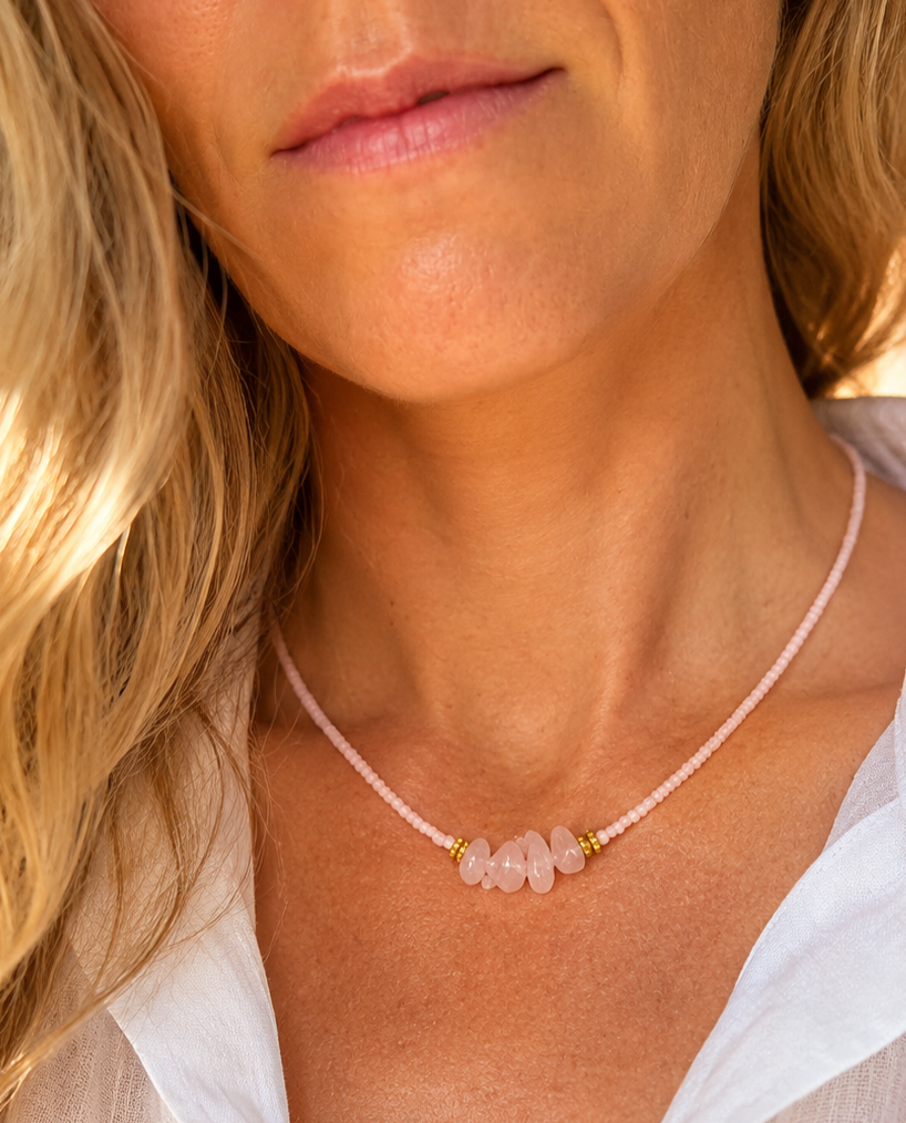 zongebruind model met blond haar draagt een zachtroze kralenketting met vier rozenkwarts edelstenen