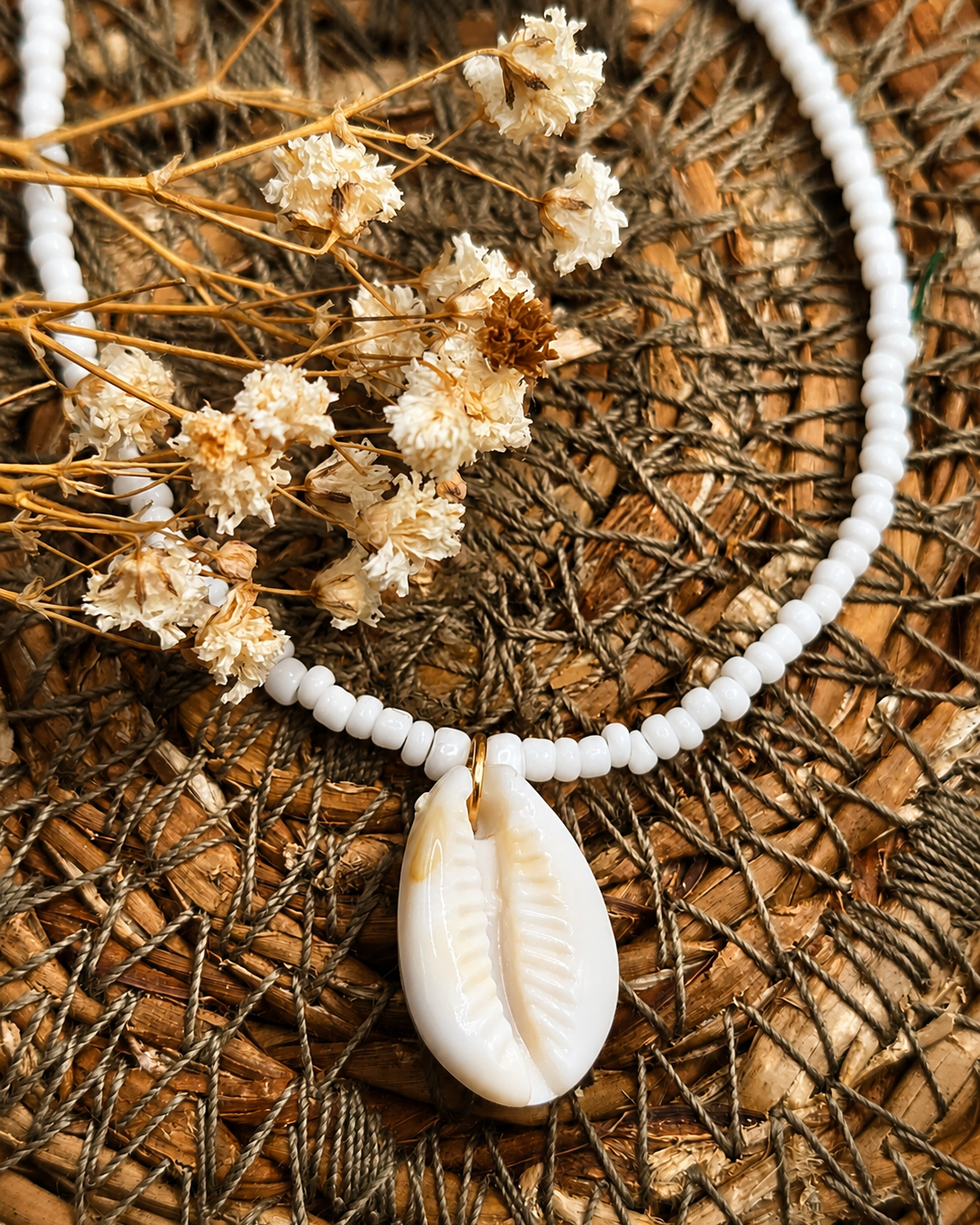 close-up foto van een wit schelpbedeltje aan een witte kralenketting op een robuuste achtergrond