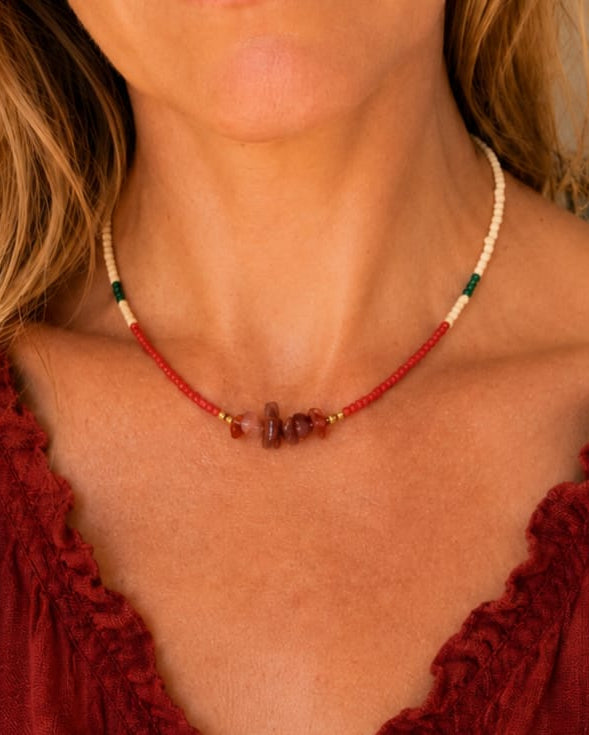 Model draagt de Siena handgemaakte rode agaat kralenketting met zandkleurige, rode en groene kralen en goudkleurige accenten.