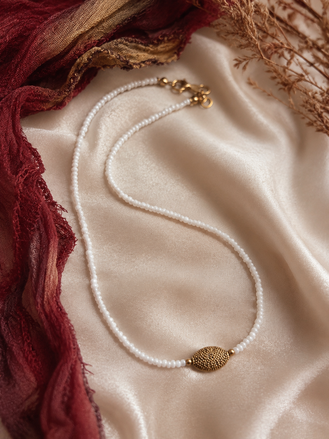 Handgemaakte witte kralenketting met goudkleurig ovaal detail en verstelbare sluiting.