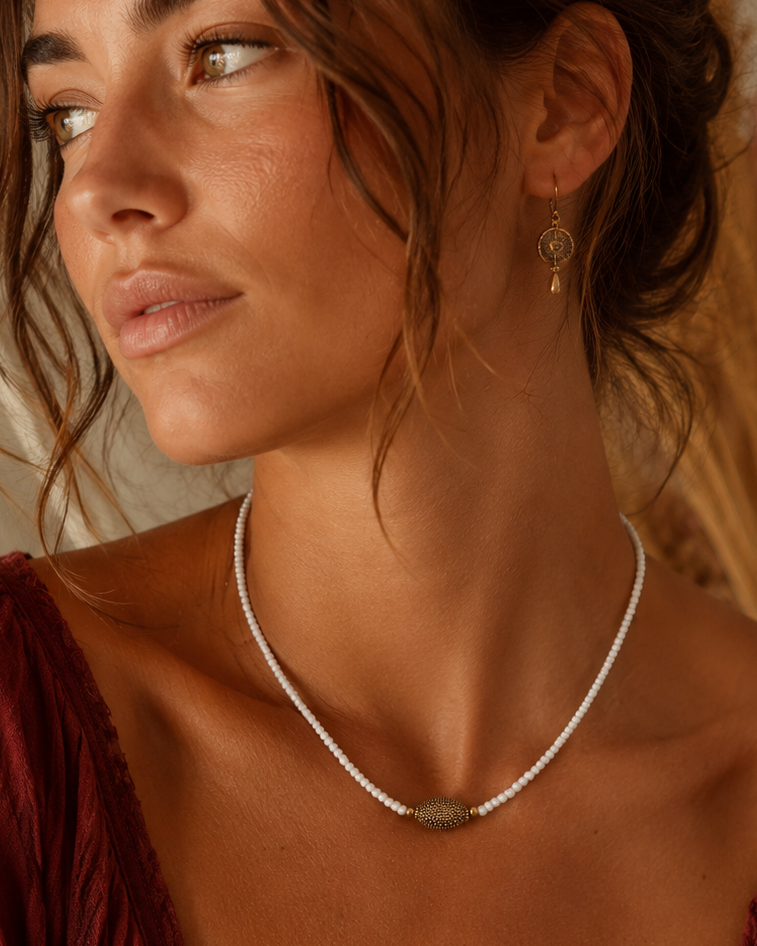 Model draagt een handgemaakte witte kralenketting met goudkleurig detail, 