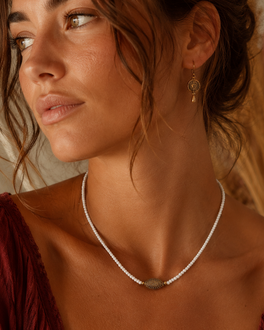 Model draagt een handgemaakte witte kralenketting met goudkleurig detail, 