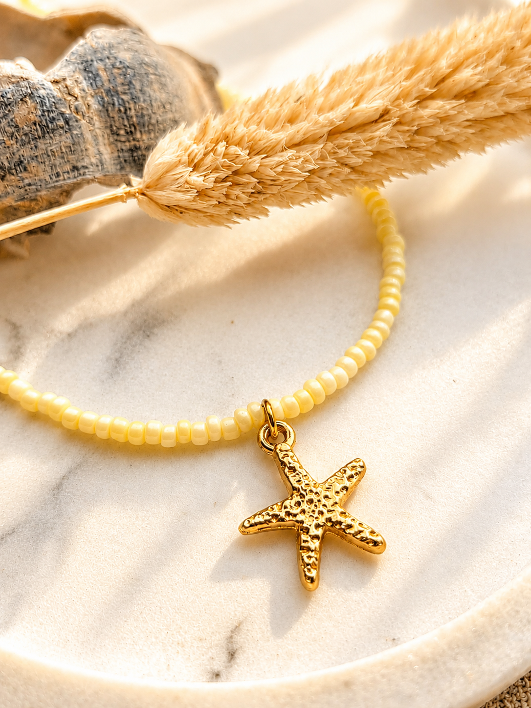 op een markeren ondergrond een close up van een gouden zeester bedel aan een zachtgele kralenketting